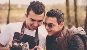 Zwei junge Männer schauen sie Fotos auf dem Display einer Kamera an.