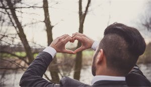 Ein junger Mann im Anzug wird von hinten gezeigt, wie er mit seinen Händen ein Herz formt.