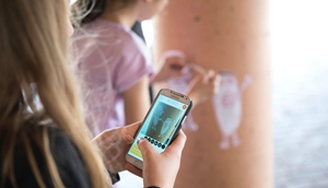 Junge Mädchen fotografieren eine Zeichnung an einer Säule mit dem Smartphone.
